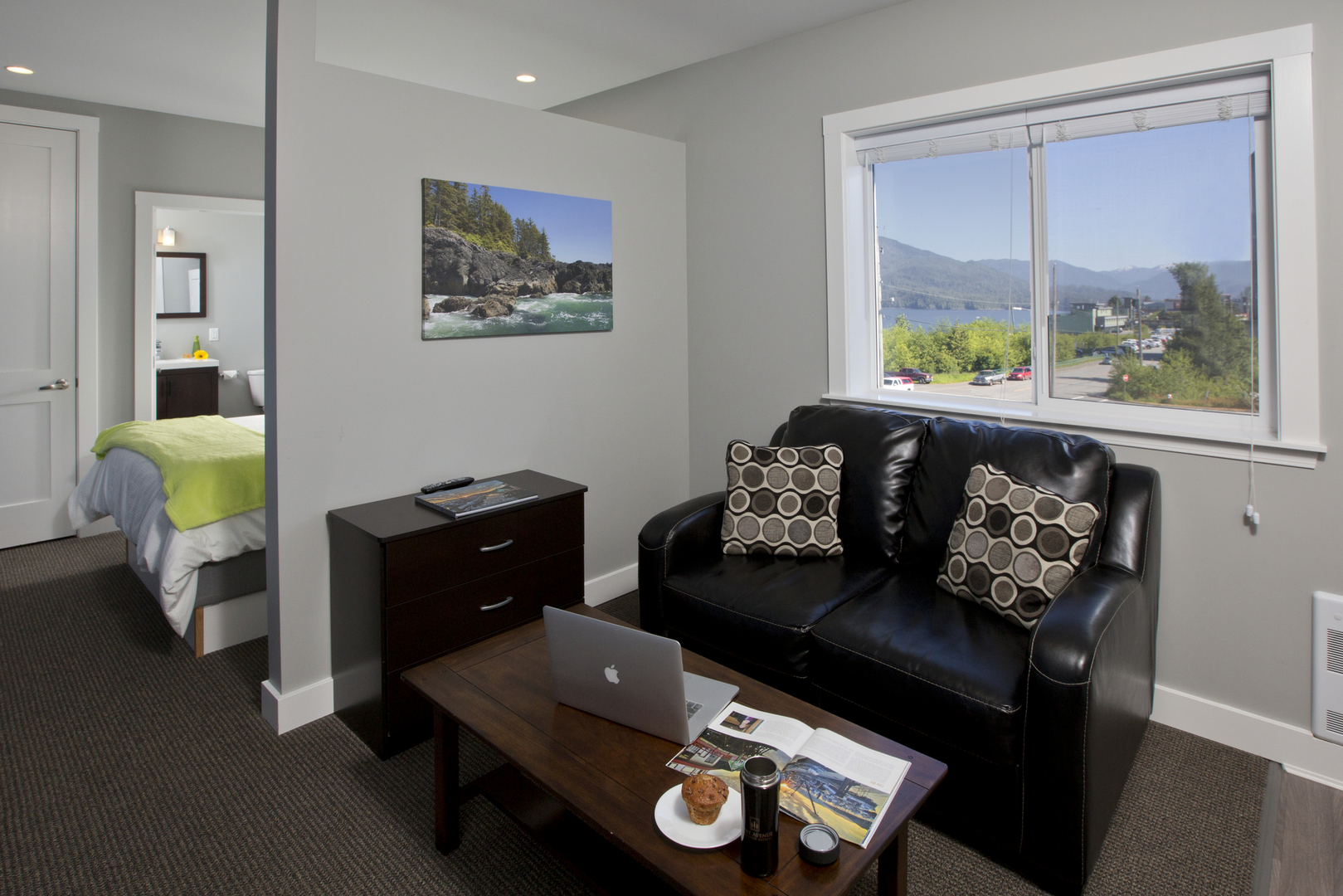 A furnished First Avenue Executive Suites living area with sofa, desk space, bedroom access, and a harbour view.